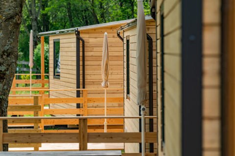Cabañas de madera con terrazas y sombrillas en Drau Camping Sachsenburg, un parque de vacaciones en Carintia.