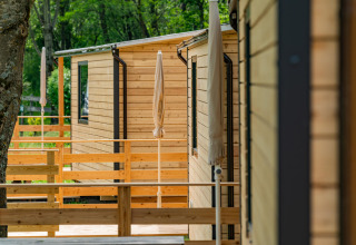 Houten chalets met terrassen en parasols op Drau Camping Sachsenburg, een vakantiepark in Karinthië, Oostenrijk.