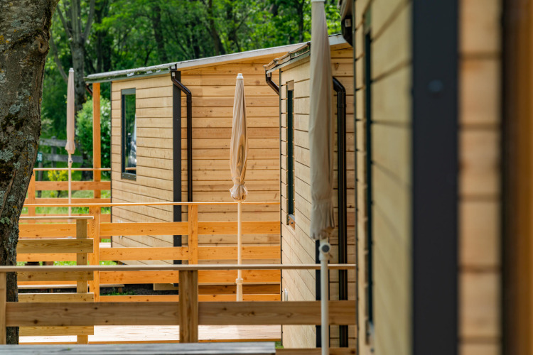 Chalets en bois avec terrasses et parasols au Drau Camping Sachsenburg, parc de vacances en Carinthie, Autriche.