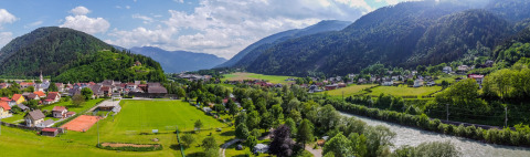 Panoramablick auf Drau Camping Sachsenburg mit Fluss, Feldern und Bergen in Kärnten, Österreich.