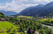 Panoramabillede af Drau Camping Sachsenburg med flod, grønne marker og bjerge i Kärnten, Østrig.