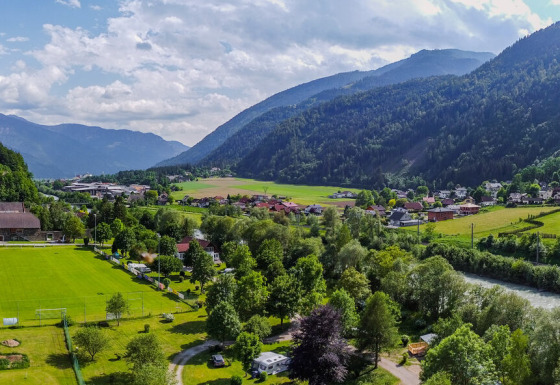 Panoramabillede af Drau Camping Sachsenburg med flod, grønne marker og bjerge i Kärnten, Østrig.