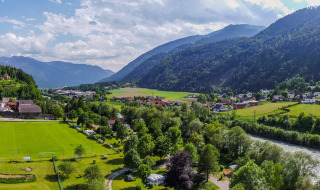 Panoramablick auf Drau Camping Sachsenburg mit Fluss, Feldern und Bergen in Kärnten, Österreich.