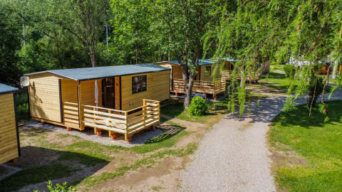 Cabañas de madera y vegetación en Drau Camping Sachsenburg, parque vacacional en Carintia, Austria, rodeado de naturaleza.