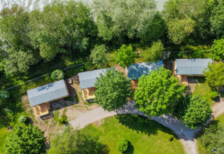 Vista aérea del parque de vacaciones Drau Camping Sachsenburg en Carintia, Austria, con cabañas y árboles verdes.