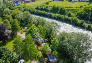 Luftfoto af Drau Camping Sachsenburg feriepark ved floden, omgivet af grønt landskab i Kärnten, Østrig.