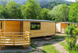 Træhytter på Drau Camping Sachsenburg i Carinthia, Østrig, omgivet af grønne træer og bjerge om sommeren.