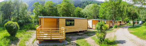 Træhytter på Drau Camping Sachsenburg i Carinthia, Østrig, omgivet af grønne træer og bjerge om sommeren.