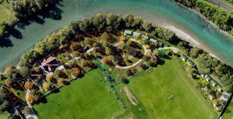 Luchtfoto van Drau Camping Sachsenburg in Karinthië, Oostenrijk, met genummerde kampeerplaatsen en rivier.