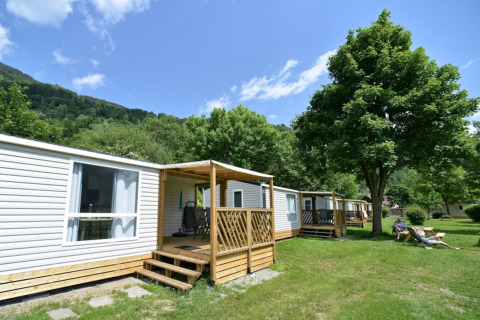 Case mobili al Drau Camping Sachsenburg in Carinzia, Austria, circondate da alberi verdi e cielo azzurro.