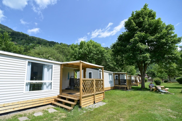 Mobil-homes au Drau Camping Sachsenburg, Carinthie, Autriche, près d’arbres verdoyants et ciel ensoleillé.