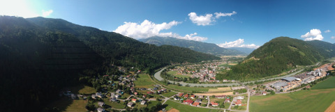 Vista panorámica del Drau Camping Sachsenburg en Carintia, Austria, con montañas, casas y un río serpenteante.