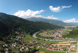 Udsigt over Drau Camping Sachsenburg feriested i Kärnten, Østrig med bjerge, flod og landsbyhus.