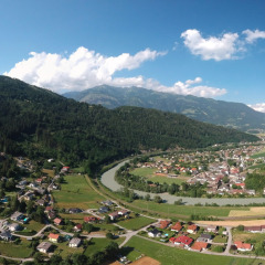 Vista panorámica del Drau Camping Sachsenburg en Carintia, Austria, con montañas, casas y un río serpenteante.