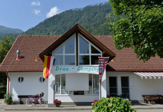 Entrance of Drau Camping Sachsenburg, with flags, mountains, and a bicycle, located in Carinthia, Austria.