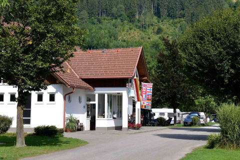 Drau Camping Sachsenburg i Kärnten, Østrig, med hovedbygning, flag, campingvogne og bjerge i baggrunden.
