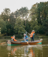 Familia pescando en un bote sobre un lago en un parque de vacaciones con glamping, rodeados de árboles.