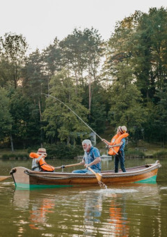 Familia pescando en un bote sobre un lago en un parque de vacaciones con glamping, rodeados de árboles.