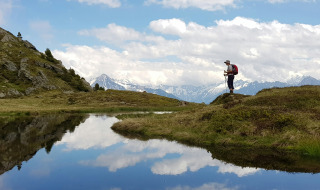 Senderista con mochila y bastones sobre una colina junto a un lago, rodeado de montañas en Kramsach, Tirol.