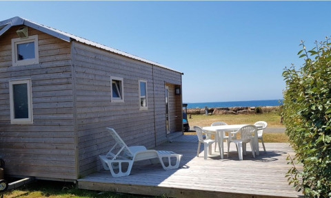 Cabaña de madera con terraza, muebles blancos y vista al mar en Camping Seasonova Les 7 Iles, Bretaña, Francia.