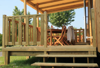 Terraza de madera con mesa y sillas en Camping Seasonova Les 7 Iles, un parque vacacional en Bretaña, Francia.