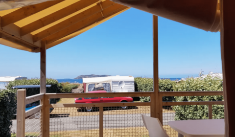 Vista desde una terraza en Camping Seasonova Les 7 Iles en Bretaña, Francia, con mar y caravanas alrededor.