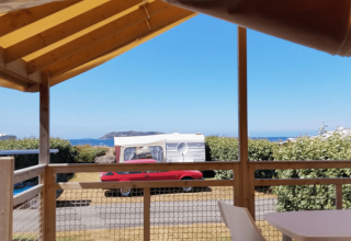 Vista da una terrazza al Camping Seasonova Les 7 Iles in Bretagna, Francia, con mare e roulotte visibili.