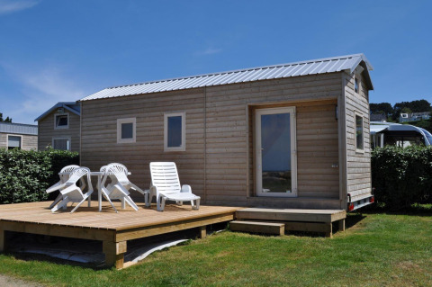 Kleine houten bungalow met terras en ligstoelen op Camping Seasonova Les 7 Iles in Bretagne, Frankrijk.