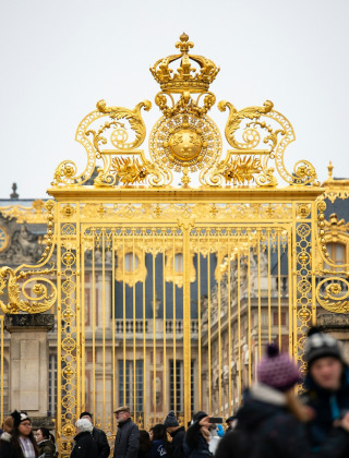 Turistas se agrupan frente a las puertas doradas del Palacio de Versalles en Versailles, Île de France, Francia.