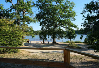 Zicht tussen de bomen op het strand en meer bij Camping Seasonova L'Etang des Bois, Centre-Val de Loire, Frankrijk.