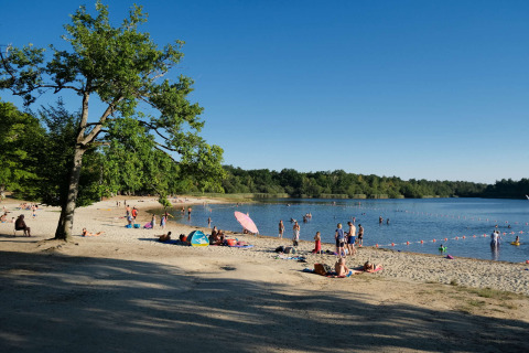 People relax on the sandy beach and swim in the lake at Camping Seasonova L'Etang des Bois in France.