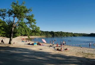 People relax on the sandy beach and swim in the lake at Camping Seasonova L'Etang des Bois in France.