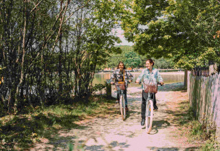 Twee personen fietsen op een zonnig pad in Camping Seasonova L'Etang des Bois, Frankrijk.