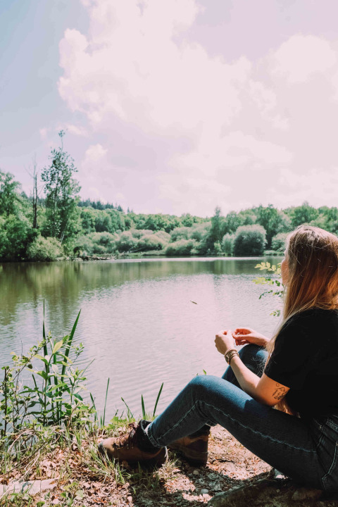 Frau sitzt am See mit Blick auf bewaldete Natur im Camping Seasonova L'Etang des Bois, Centre-Val de Loire.