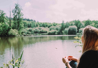 Vrouw zit ontspannen aan een meer bij Camping Seasonova L'Etang des Bois, omringd door groen in Centre-Val de Loire.