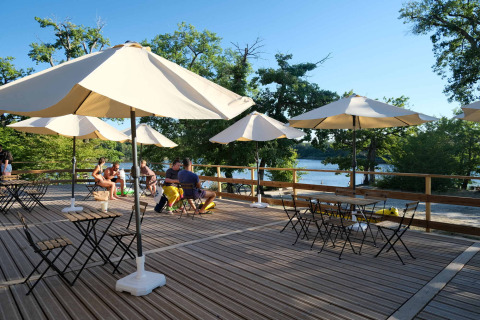 Terraza exterior con sombrillas, mesas y sillas en Camping Seasonova L'Etang des Bois, Centre-Val de Loire, Francia.