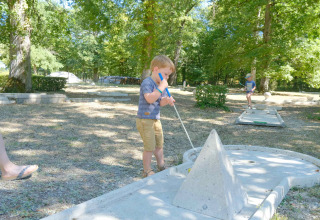 Twee kinderen spelen minigolf in de schaduw van bomen op Camping Seasonova L'Etang des Bois, Frankrijk.