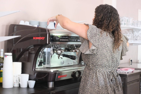 Vrouw maakt koffie bij een espressomachine op Camping Seasonova L'Etang des Bois, Centre-Val de Loire, Frankrijk.