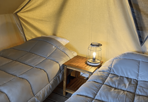 Dos camas individuales en tienda tipi con mesa y lámpara, Bivouac Nomade en Camping Seasonova L'Etang des Bois, Francia.