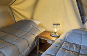 Due letti singoli in una tenda teepee con tavolino e lampada, Bivouac Nomade al Camping Seasonova L'Etang des Bois, Francia.