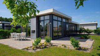 Lodge Pavilion moderno con grandes ventanales, patio y muebles de jardín bajo un cielo azul claro.