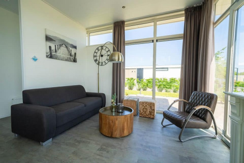 Moderne woonkamer in Pavilion, EuroParcs Veluwemeer met grote ramen, donkere bank en houtentafel in Nederland.