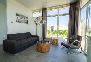 Moderne stue i Pavilion på EuroParcs Veluwemeer med store vinduer, sort sofa og træbord i Holland.