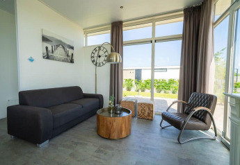 Sala moderna en Pavilion de EuroParcs Veluwemeer, Países Bajos, con grandes ventanas, sofá oscuro y mesa de madera.