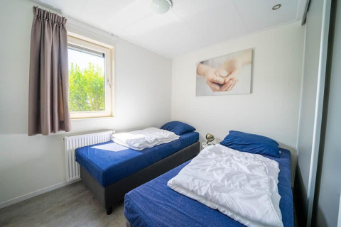 Habitación con dos camas individuales y ropa de cama azul en Pavilion, EuroParcs Veluwemeer, Países Bajos, luz solar.