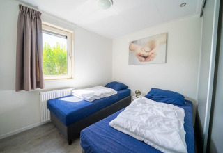 Zimmer mit zwei Einzelbetten und blauer Bettwäsche im Pavilion, EuroParcs Veluwemeer, Niederlande, sonnig.