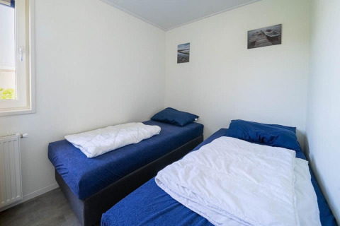 Dormitorio con dos camas individuales, ropa de cama azul y paredes blancas en Pavilion en EuroParcs Veluwemeer.
