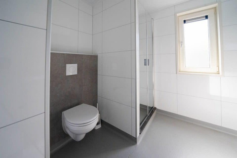 Salle de bains moderne avec toilettes suspendues, douche et fenêtre au Pavilion d'EuroParcs Veluwemeer.