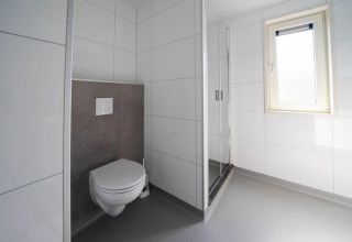 Salle de bains moderne avec toilettes suspendues, douche et fenêtre au Pavilion d'EuroParcs Veluwemeer.
