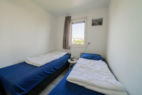 Habitación con dos camas individuales, ropa de cama azul, ventana y mesa pequeña en el Pavilion de EuroParcs Veluwemeer.